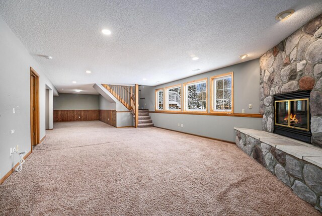 unfurnished living room featuring a stone fireplace, a textured ceiling, and light carpet