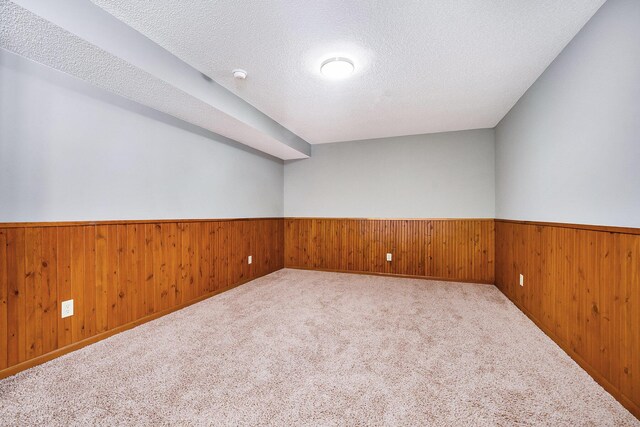 unfurnished room featuring wood walls, light colored carpet, and a textured ceiling