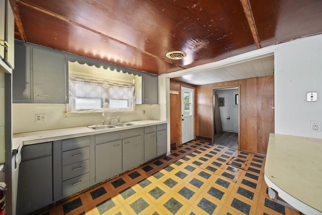 kitchen featuring gray cabinetry, wooden walls, and sink