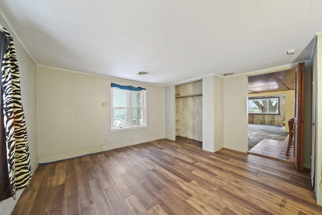 unfurnished bedroom with hardwood / wood-style flooring, wooden walls, and multiple windows