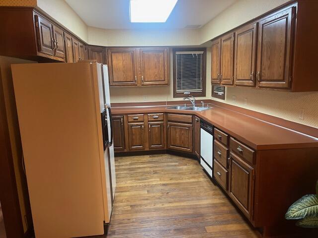 kitchen featuring light wood-type flooring, white appliances, a skylight, and sink