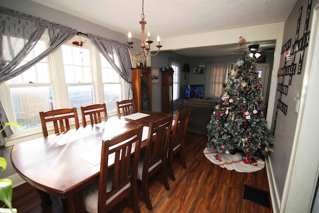 dining space with ceiling fan with notable chandelier, a textured ceiling, a wealth of natural light, and dark wood-type flooring