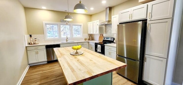 kitchen featuring sink, stainless steel appliances, wall chimney range hood, decorative light fixtures, and white cabinets