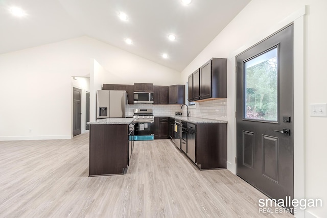 kitchen featuring light wood-type flooring, light stone counters, stainless steel appliances, a kitchen island, and lofted ceiling