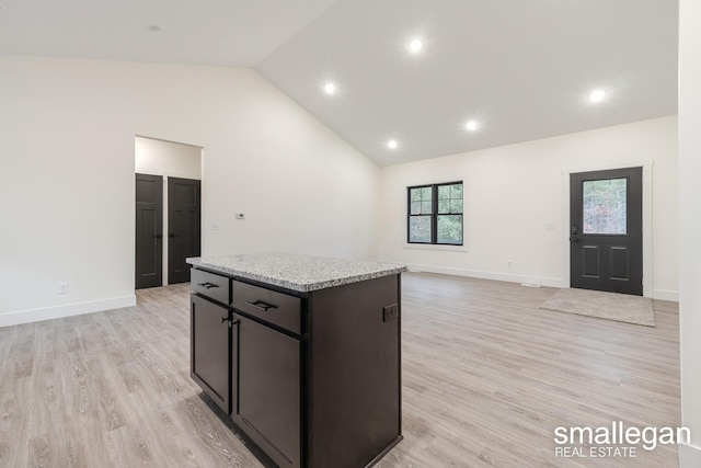 kitchen with a center island, high vaulted ceiling, light stone countertops, light wood-type flooring, and dark brown cabinetry