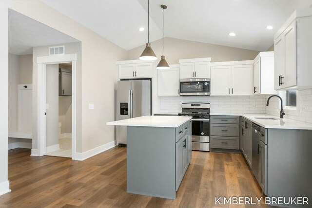 kitchen with sink, stainless steel appliances, vaulted ceiling, gray cabinets, and a kitchen island