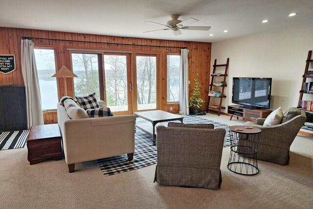 carpeted living room featuring ceiling fan and wooden walls