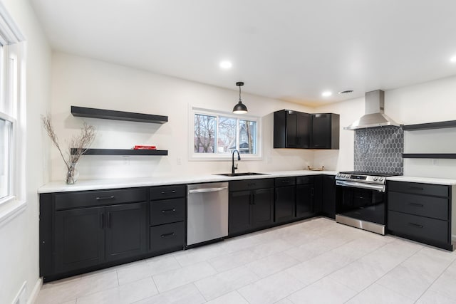 kitchen featuring stainless steel appliances, sink, wall chimney range hood, light tile patterned floors, and decorative light fixtures