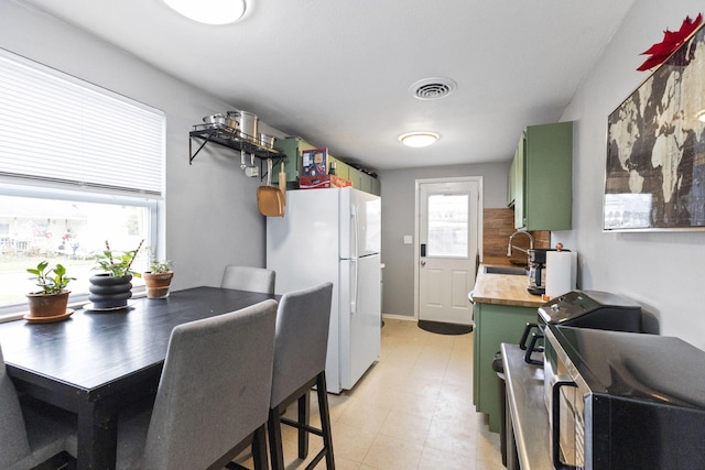 kitchen featuring white fridge, sink, butcher block countertops, and green cabinetry