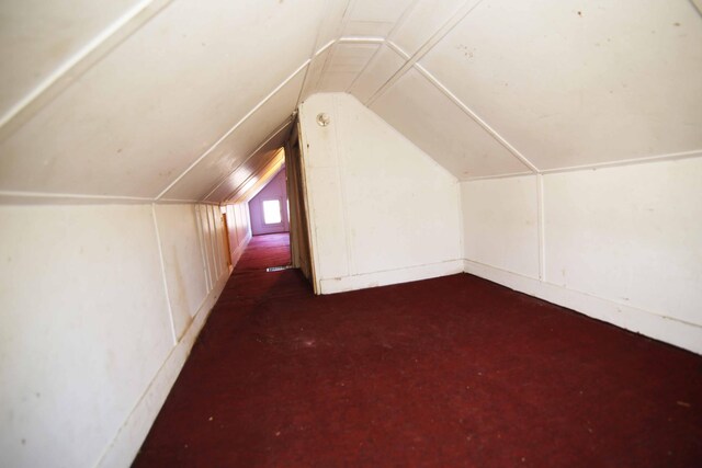 additional living space featuring dark colored carpet and lofted ceiling