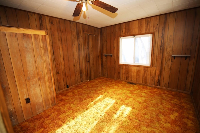 carpeted empty room featuring ceiling fan and wood walls