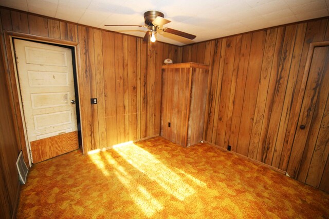 carpeted spare room with wooden walls and ceiling fan