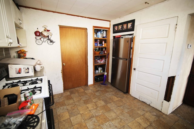 kitchen featuring white gas range, stainless steel fridge, and white cabinets