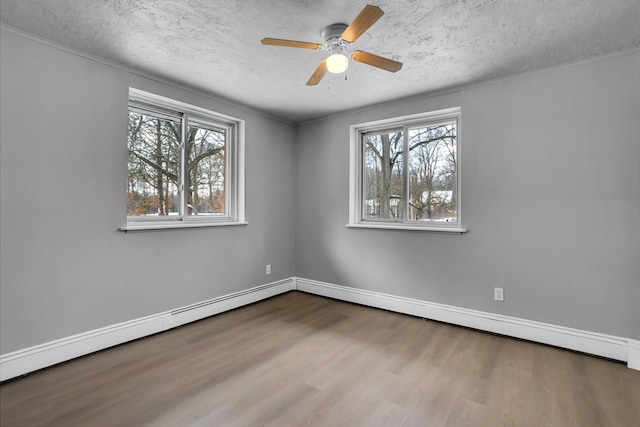 empty room with plenty of natural light, a baseboard radiator, a textured ceiling, and light hardwood / wood-style flooring