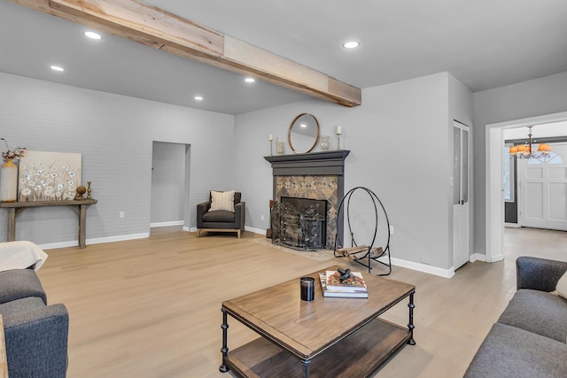 living room featuring beamed ceiling, a stone fireplace, wood-type flooring, and a chandelier