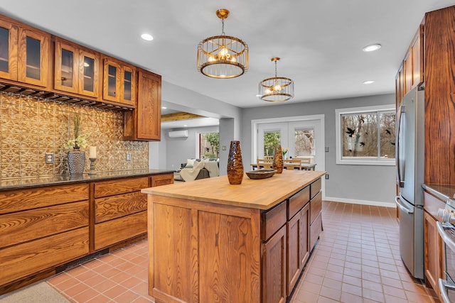 kitchen featuring a center island, backsplash, an inviting chandelier, hanging light fixtures, and stainless steel refrigerator