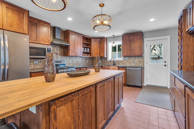 kitchen with stainless steel appliances, wall chimney range hood, wooden counters, a chandelier, and decorative light fixtures