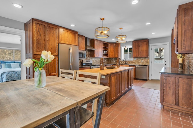 kitchen featuring pendant lighting, sink, wall chimney exhaust hood, light tile patterned flooring, and stainless steel appliances