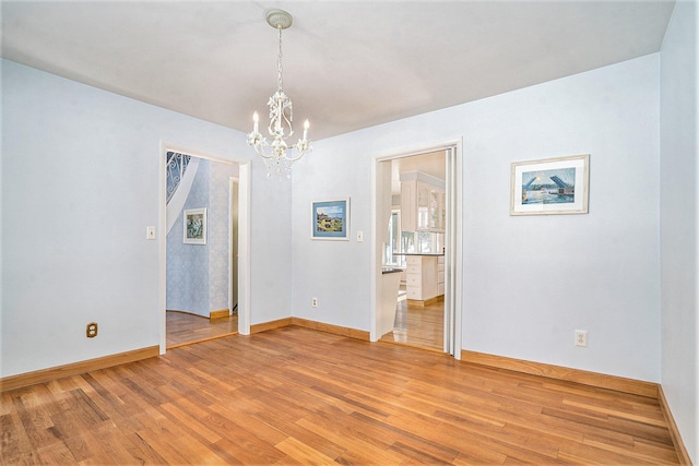 spare room with an inviting chandelier and wood-type flooring