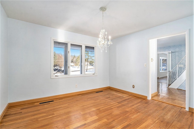 empty room featuring an inviting chandelier, plenty of natural light, and light wood-type flooring