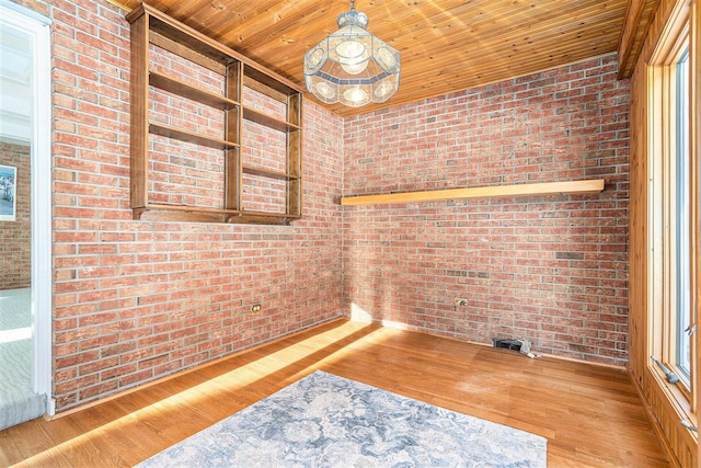 empty room featuring light hardwood / wood-style flooring, wooden ceiling, and brick wall