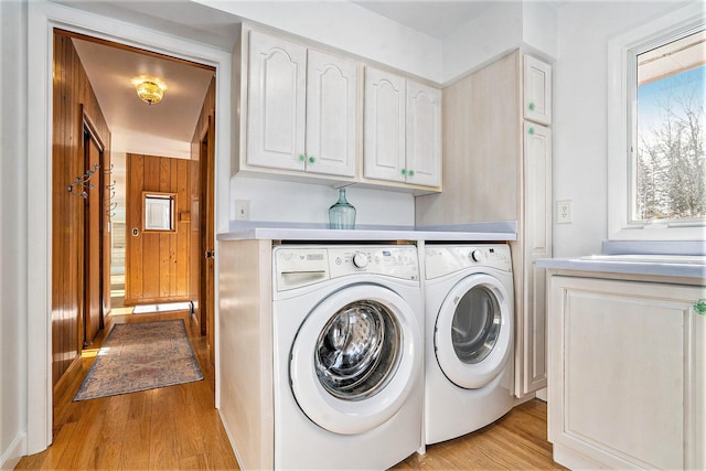 clothes washing area featuring cabinets, washing machine and dryer, and light wood-type flooring