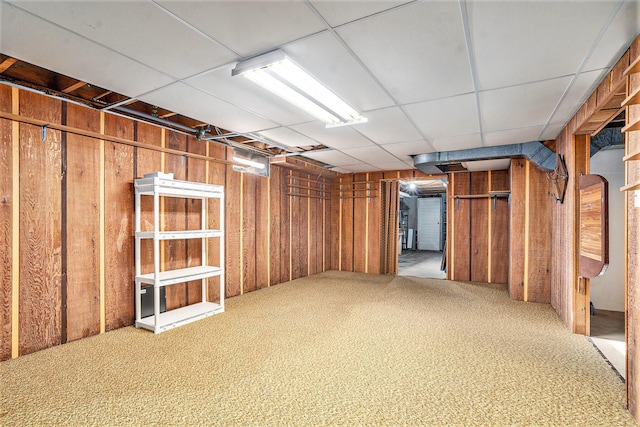 basement with a paneled ceiling, carpet floors, and wood walls