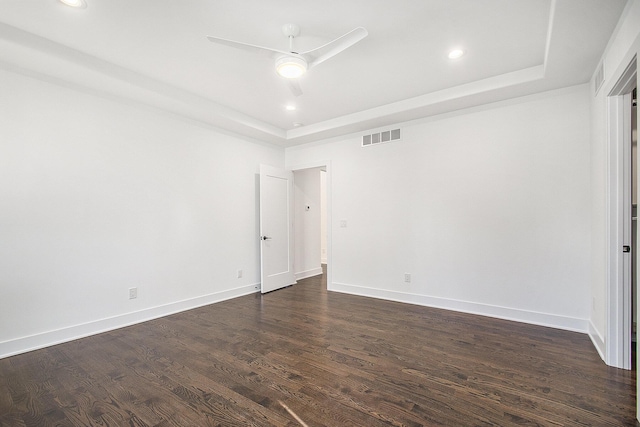 empty room with dark hardwood / wood-style floors, ceiling fan, and a tray ceiling