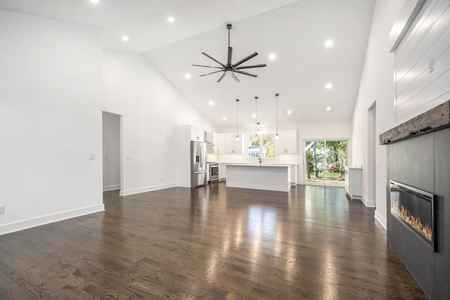 unfurnished living room with ceiling fan, dark wood-type flooring, and high vaulted ceiling