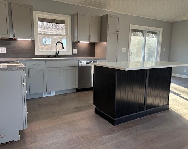 kitchen featuring decorative backsplash, a kitchen island, stainless steel dishwasher, and light wood-type flooring