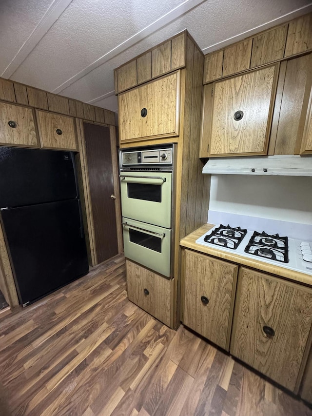 kitchen with wooden walls, black fridge, double oven, and dark wood-type flooring