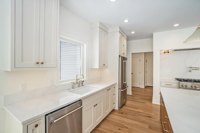 kitchen with light stone counters, sink, high quality appliances, white cabinets, and light hardwood / wood-style floors