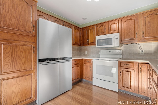 kitchen with decorative backsplash, light wood-type flooring, and white appliances