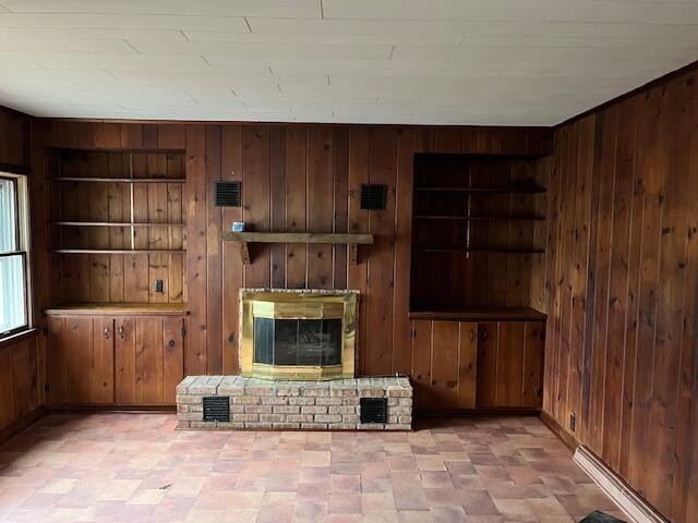 unfurnished living room with a fireplace, built in shelves, and wood walls