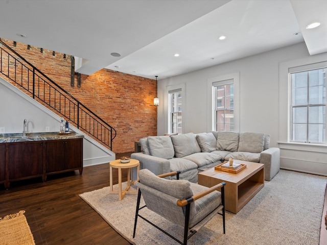 living room with dark hardwood / wood-style flooring, brick wall, and sink