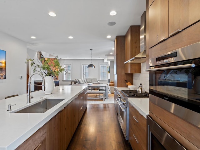 kitchen with stainless steel appliances, wall chimney range hood, sink, pendant lighting, and dark hardwood / wood-style floors