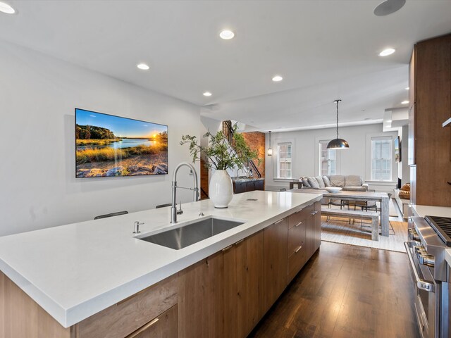 kitchen featuring sink, dark hardwood / wood-style flooring, decorative light fixtures, range with two ovens, and a kitchen island with sink