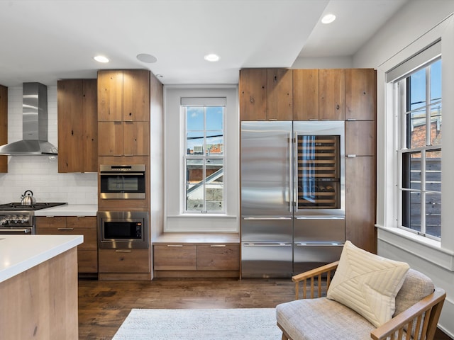 kitchen with built in appliances, dark hardwood / wood-style flooring, wall chimney exhaust hood, and a healthy amount of sunlight