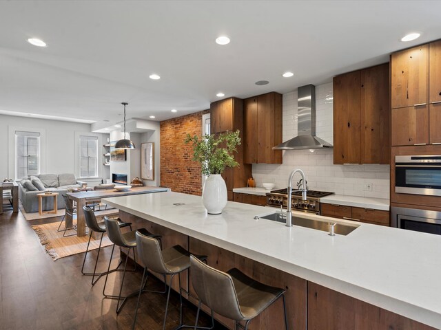 kitchen featuring wall chimney exhaust hood, decorative light fixtures, dark wood-type flooring, and a breakfast bar