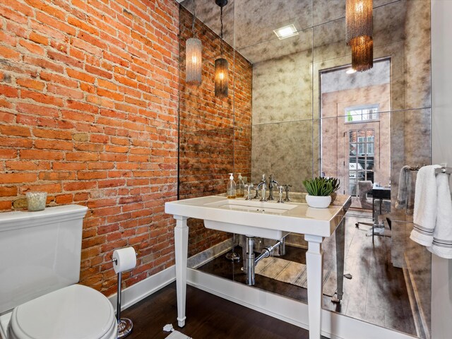 bathroom with wood-type flooring, toilet, and brick wall