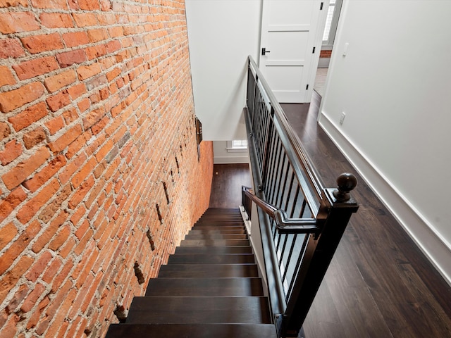 staircase with wood-type flooring and brick wall