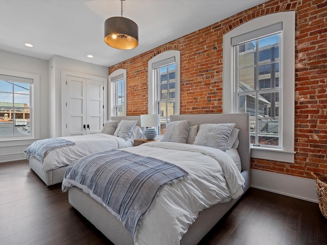 bedroom featuring dark hardwood / wood-style flooring and brick wall