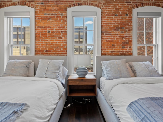 bedroom with wood-type flooring, multiple windows, and brick wall