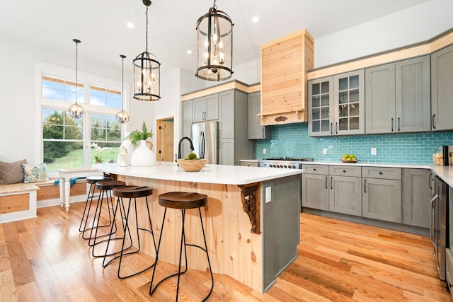 kitchen featuring backsplash, gray cabinets, a center island with sink, appliances with stainless steel finishes, and light wood-type flooring