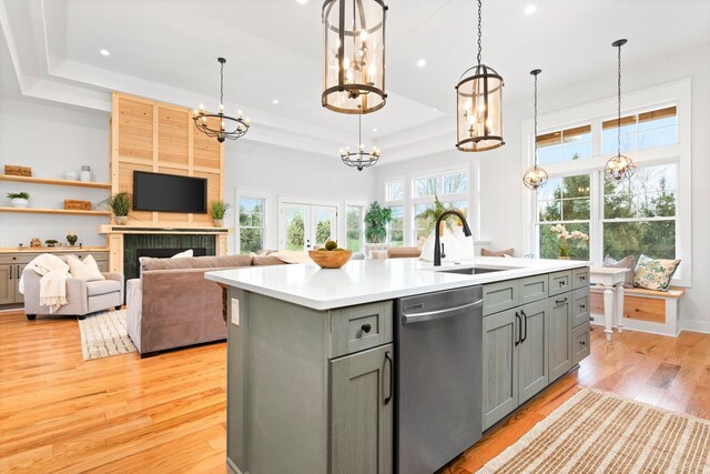 kitchen with light wood-type flooring, sink, a center island with sink, dishwasher, and a tiled fireplace