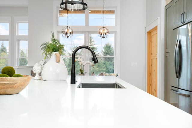 interior details featuring a chandelier, pendant lighting, stainless steel refrigerator, and sink