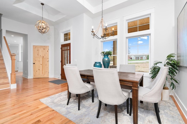 dining area with a tray ceiling, a towering ceiling, light hardwood / wood-style floors, and an inviting chandelier