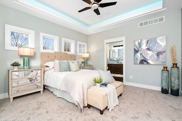 carpeted bedroom with a tray ceiling, ensuite bathroom, and ceiling fan