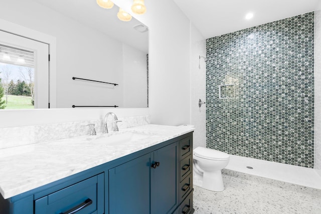 bathroom with tiled shower, vanity, and toilet