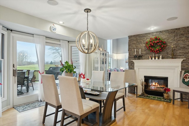 dining area featuring light hardwood / wood-style flooring, a stone fireplace, and a notable chandelier